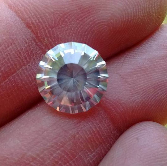 A round, faceted, colorless gem positioned on someone's fingers for viewing.